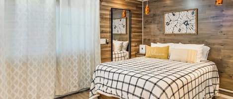 Un dormitorio con cama, suelo de madera, un espejo y una obra de arte colgada en la pared.