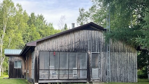 Une cabane en bois rustique, dotée d’un grand porche grillagé et d’une porte en métal.