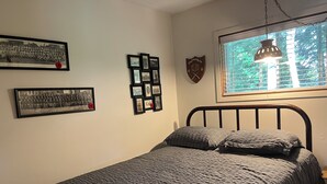 Une chambre à coucher avec un lit, des tableaux encadrés accrochés au mur et une fenêtre donnant sur un paysage.