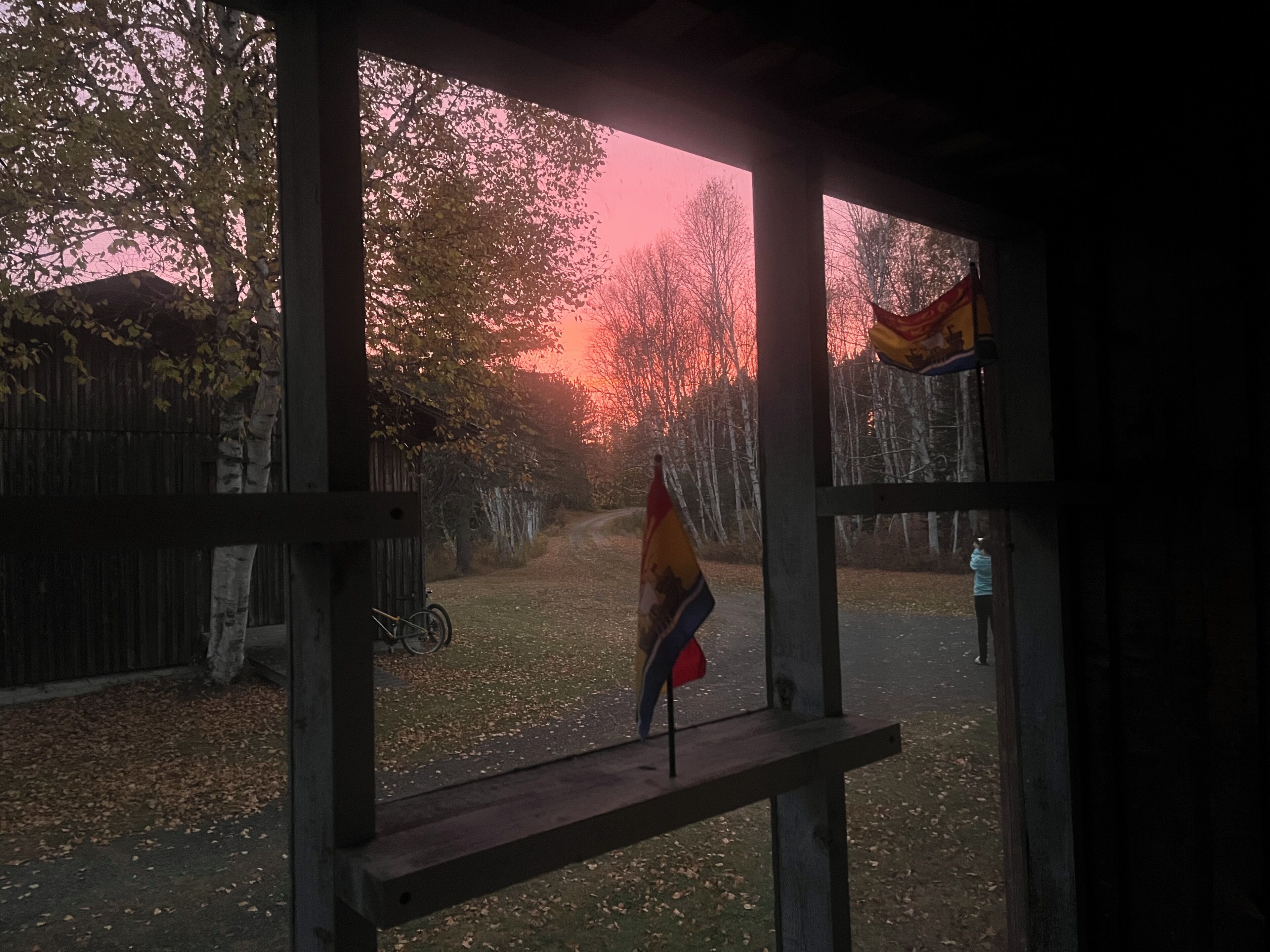 Vista a través de una ventana con una valla de madera, una bandera y una bicicleta.