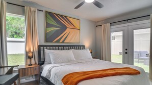 Ein Schlafzimmer mit Bett, Nachttisch, Lampe, Deckenventilator und Blick ins Freie.