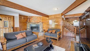 Una sala de estar acogedora con chimenea, paredes de madera y una escalera que sube a otro nivel.