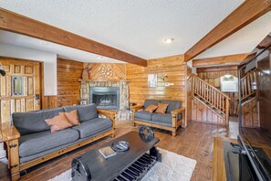 A cozy living room with a fireplace, wooden walls, and a staircase leading to another level.