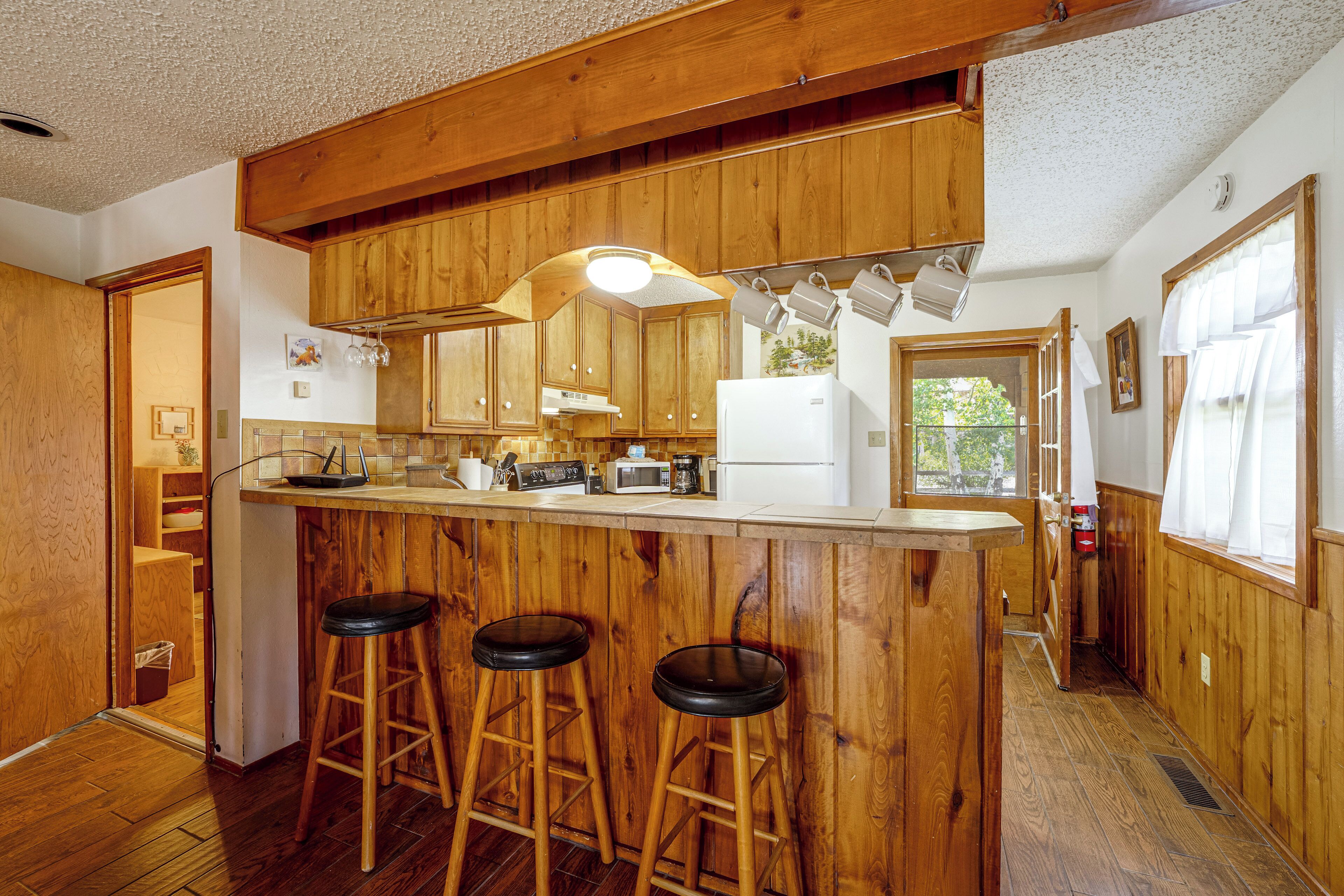 Una cocina con armarios de madera, una barra con taburetes y un microondas.