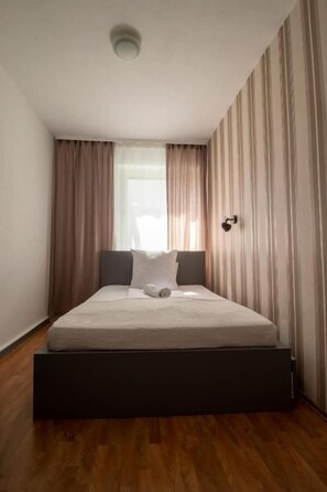 Uma cama de solteiro com cabeceira, mesa de cabeceira e janela com cortinas.