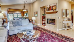 A spacious living room with a fireplace, a sofa set, a coffee table, and a bookshelf. - Work & Play in Indio: Golf Course Home w/ Patio (Indio)