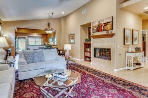 A spacious living room with a fireplace, a sofa set, a coffee table, and a bookshelf. - Work & Play in Indio: Golf Course Home w/ Patio (Indio)