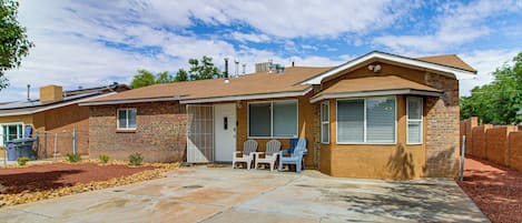 A single-story house with a brick facade, a front porch with two Adirondack chairs, and a clear sky.