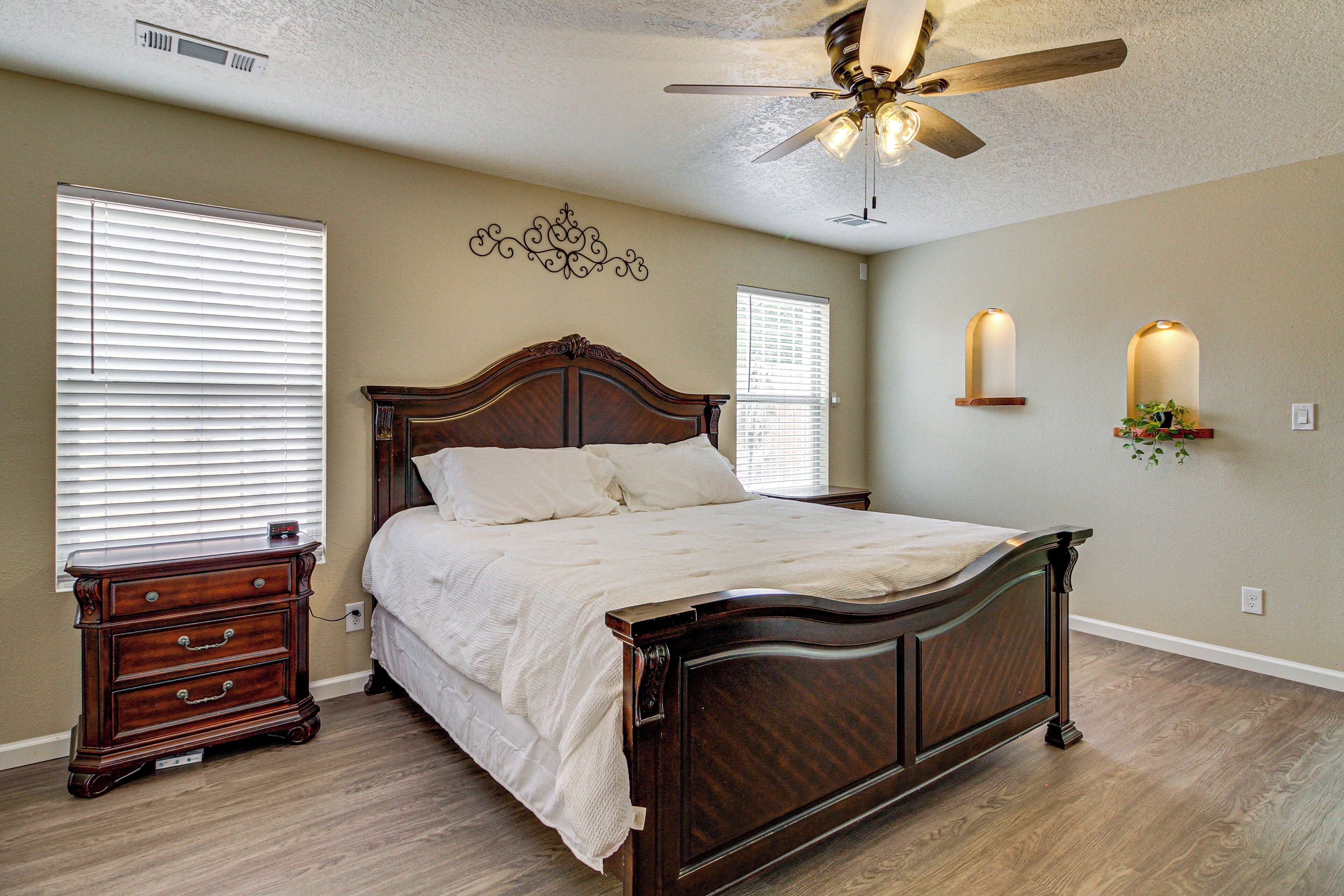 A bedroom with a wooden bed, a nightstand, a dresser, a ceiling fan, and two wall-mounted sconces.