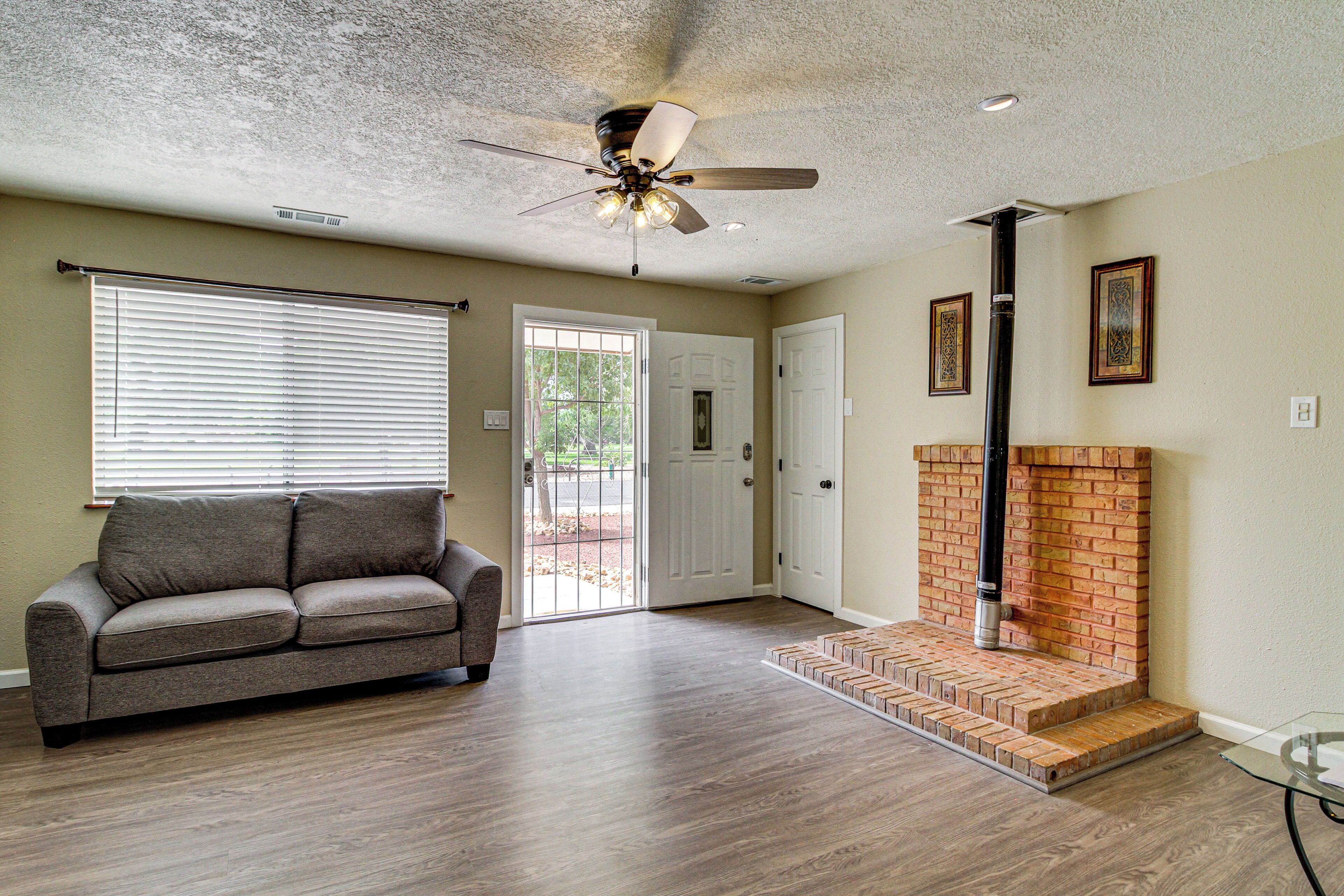 A living room with a ceiling fan, a fireplace, a sofa, and a door leading outside.