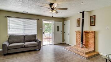 A living room with a ceiling fan, a fireplace, a sofa, and a door leading outside.
