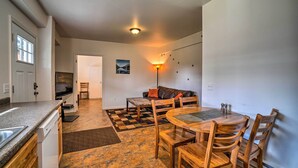 A compact kitchen with a dishwasher, a dining area with a wooden table and chairs, a sofa, and a checkered rug.