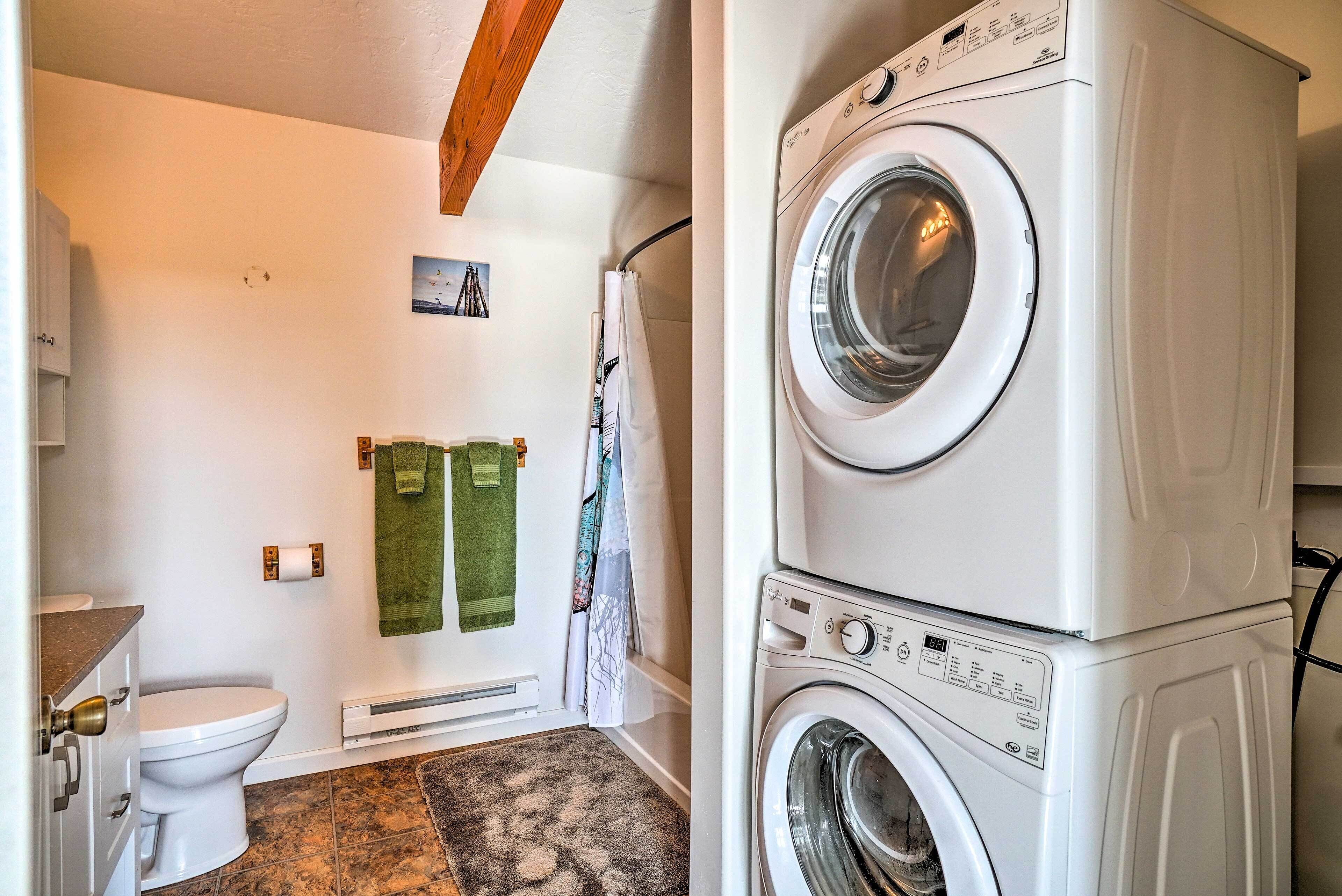 A laundry room with stacked washers and dryers, a toilet, and a shower curtain.