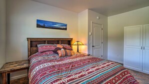 A bedroom with a wooden bed, patterned bedding, a nightstand, a lamp, a door, and a wardrobe.