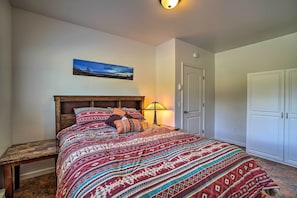 A bedroom with a wooden bed, patterned bedding, a nightstand, a lamp, a door, and a wardrobe.