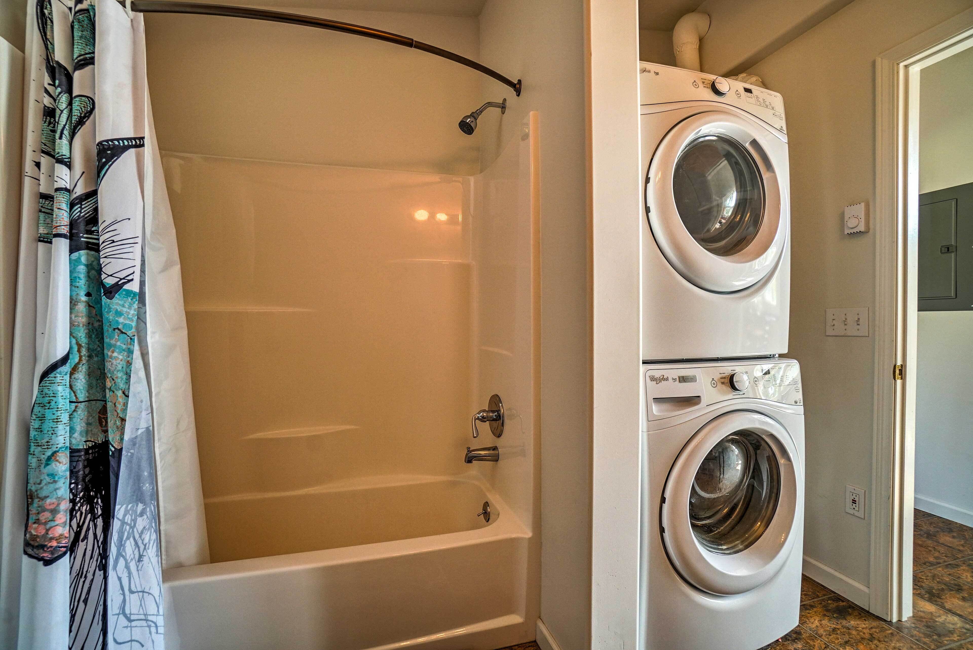 A bathroom with a bathtub, a shower, and a stacked washer and dryer.