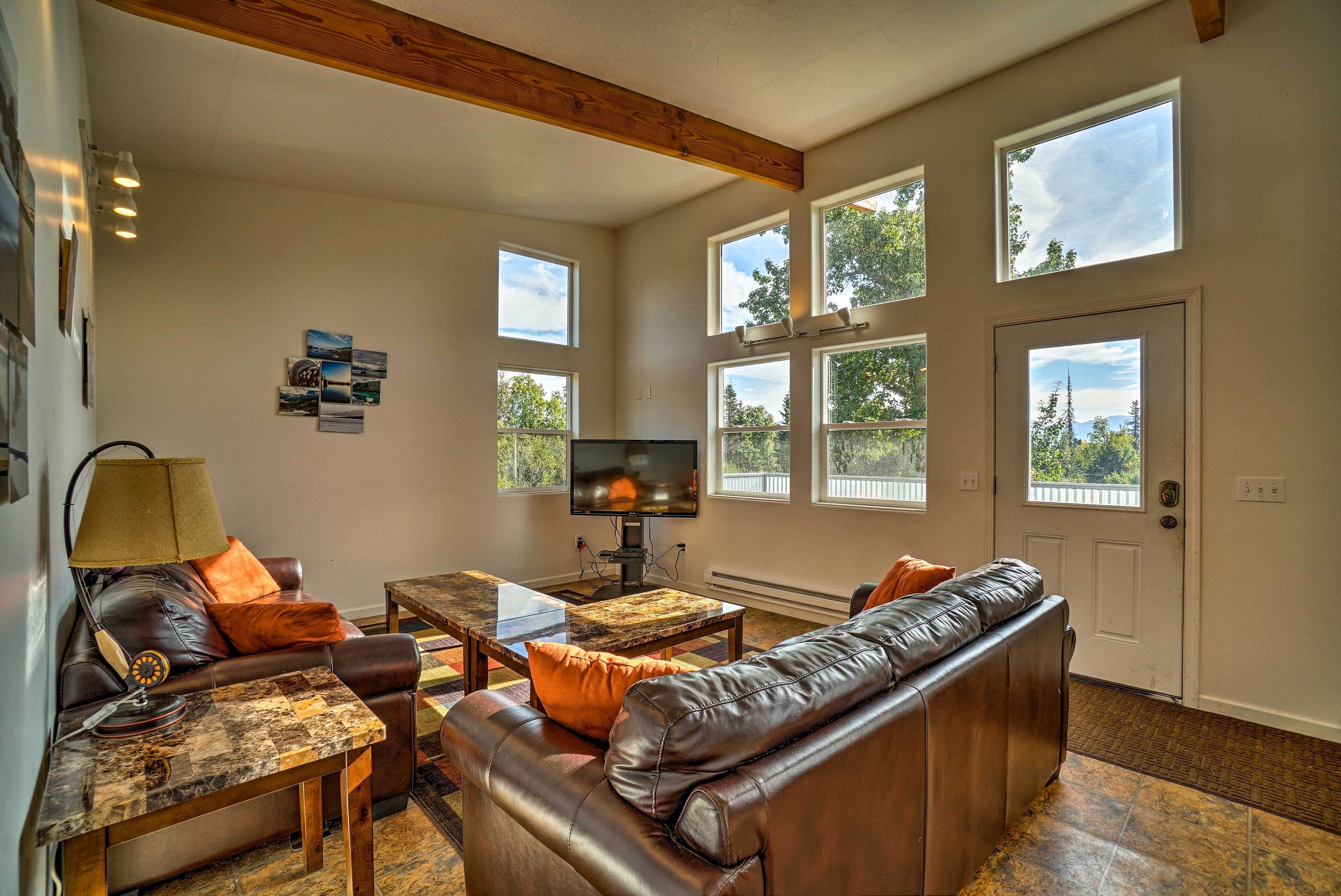 A spacious living room with a large window, a flat-screen TV, leather sofas, and a coffee table.