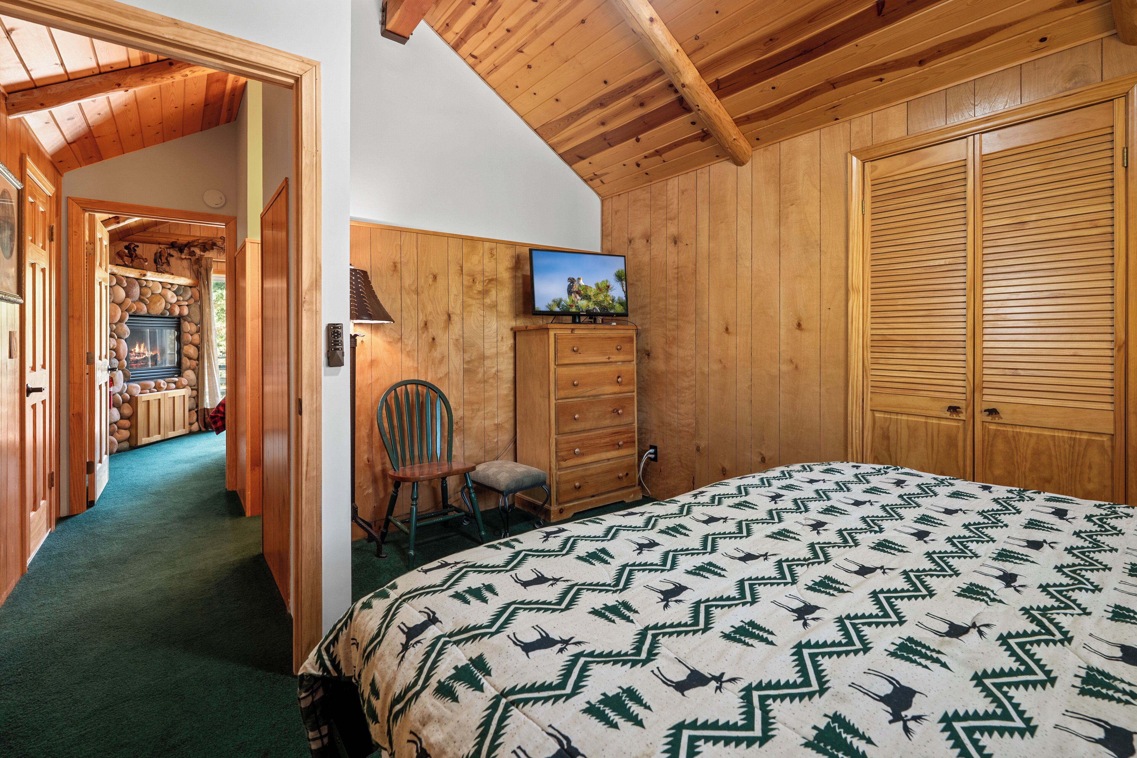 A room with a bed, a wooden wardrobe, a television on the wall, and a fireplace.