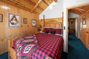 Un dormitori amb panells de fusta, un llit, obra d'art emmarcada i una porta que dona a una altra habitació.