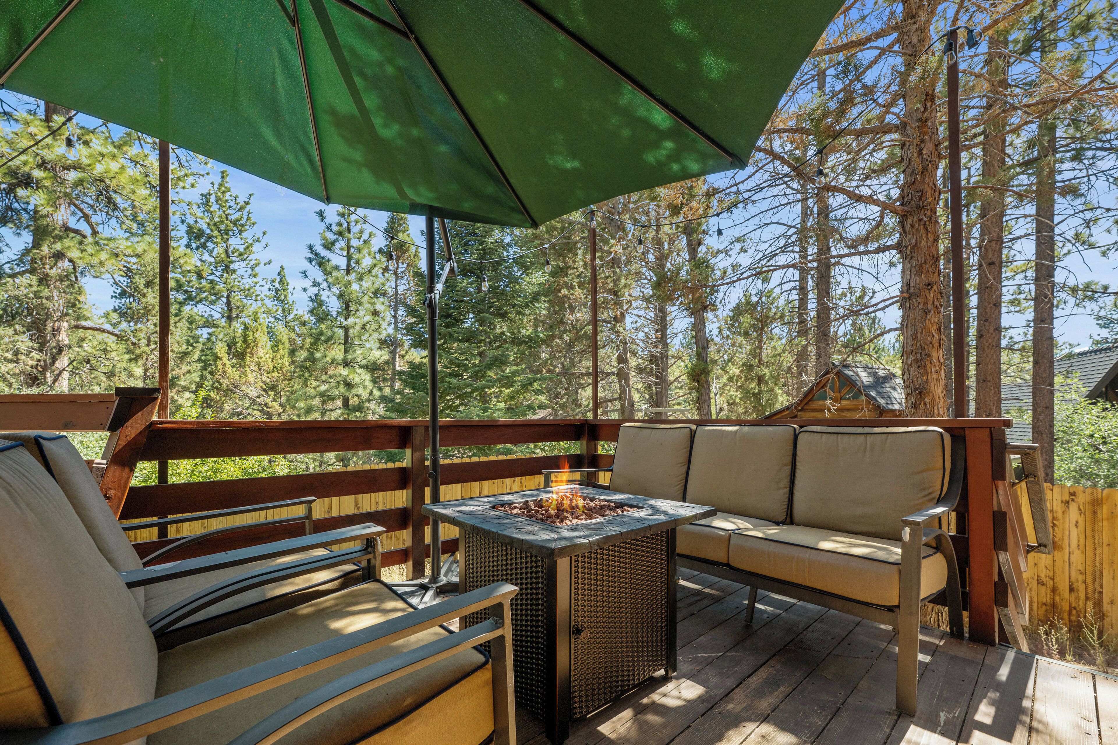 An outdoor deck with a fire pit, seating, and a view of a forest.