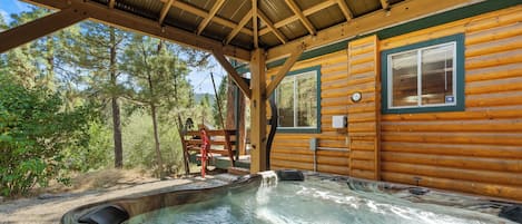Una cabaña de madera con jacuzzi, ventana y vistas al bosque.