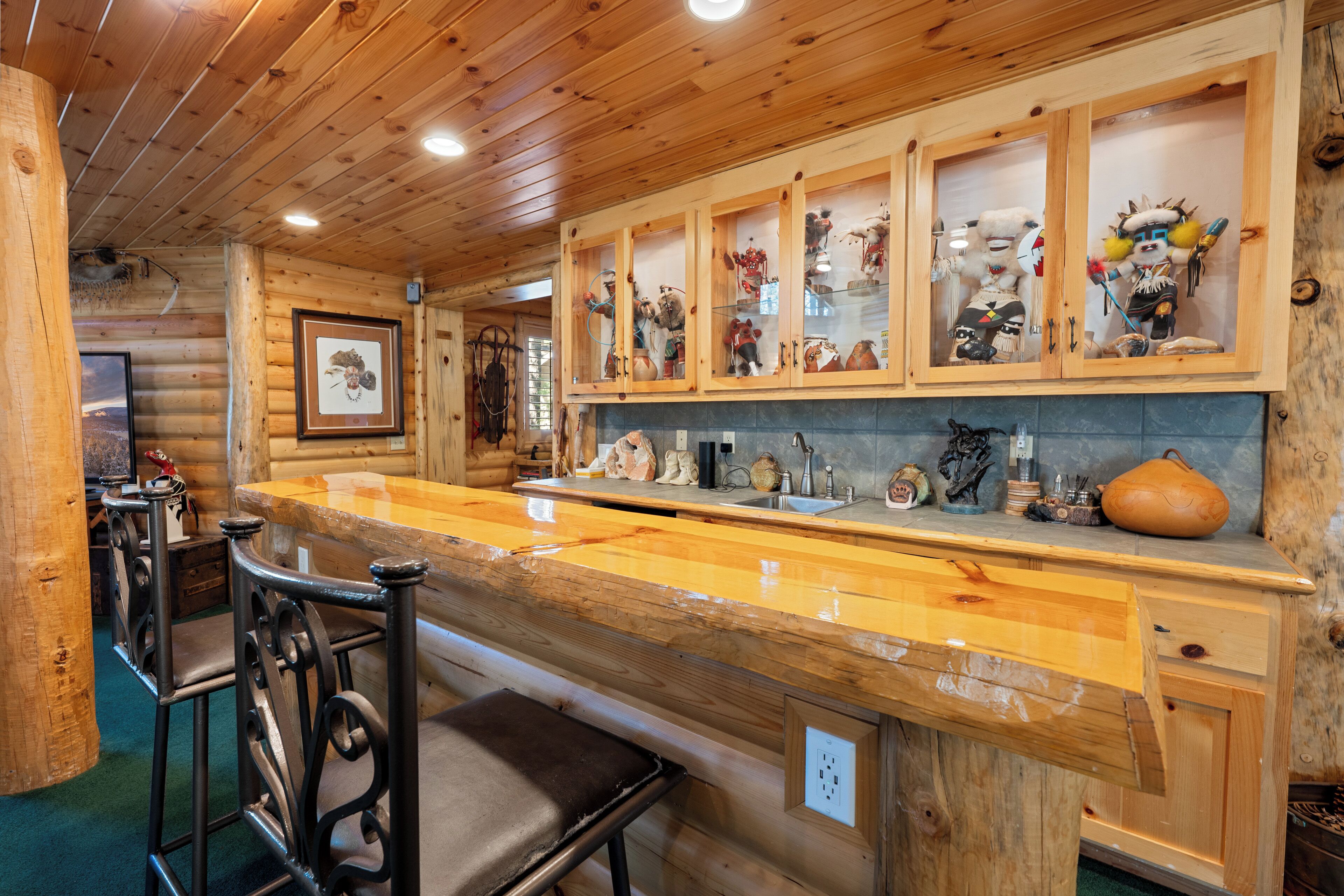 Interior de madera con zona de bar, que incluye barra, taburetes y un mueble con adornos.