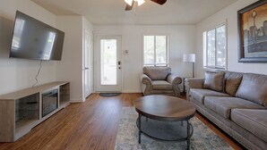 A living room with a flat-screen TV, a ceiling fan, a sofa, a coffee table, and a door with a window. - Walk to Med Center! Extended Wilmington Condo (Wilmington)