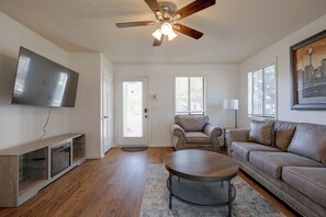 Ein Wohnzimmer mit Flachbildfernseher, Deckenventilator, Sofa, Couchtisch und einer Tür mit Fenster.