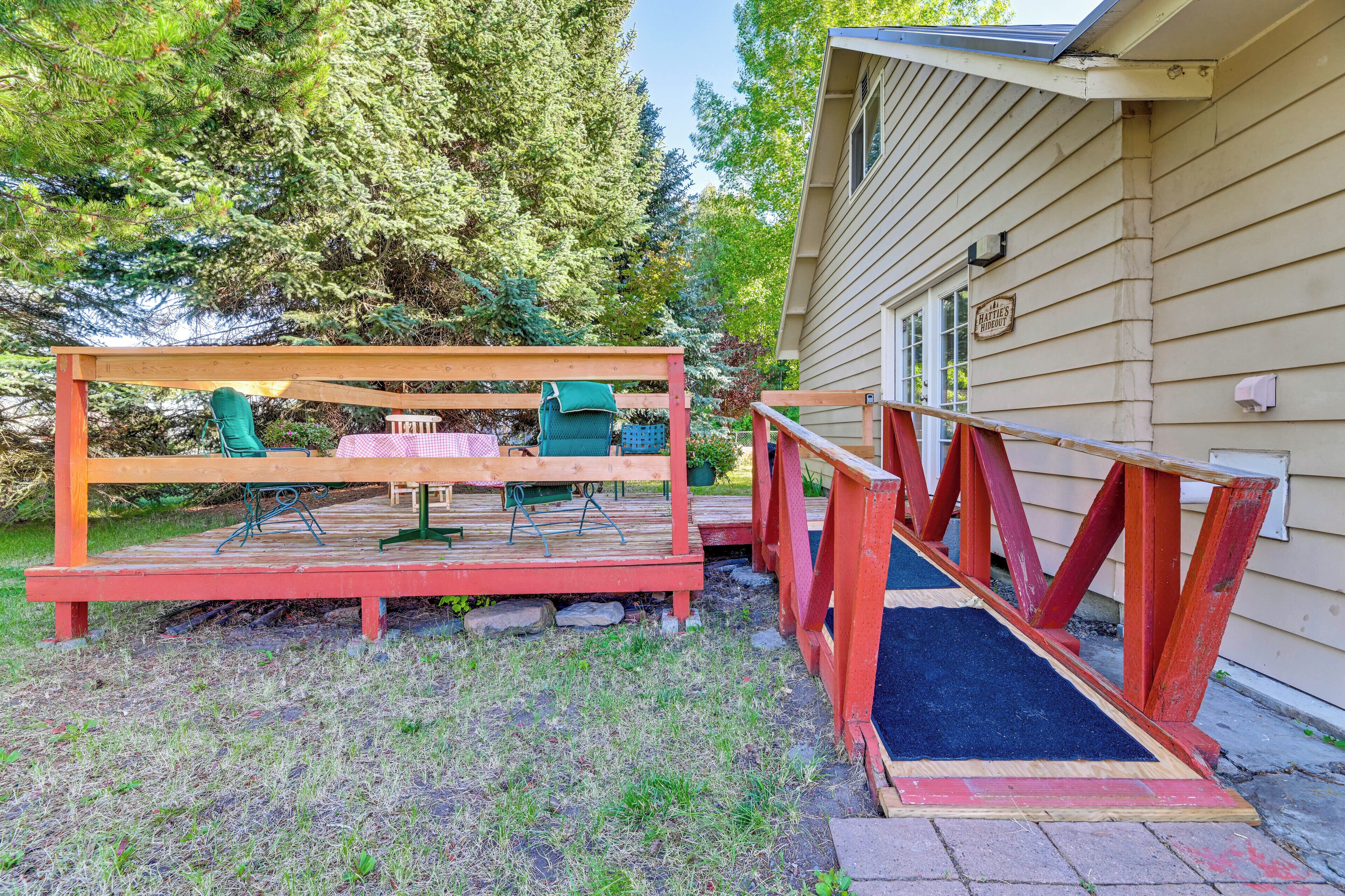 Eine Holzterrasse mit Tisch und Stühlen, ein kleiner Gartenbereich mit einem Topfpflanzen und ein Haus mit dem Schild 'HATTIE'S HIDEOUT'.