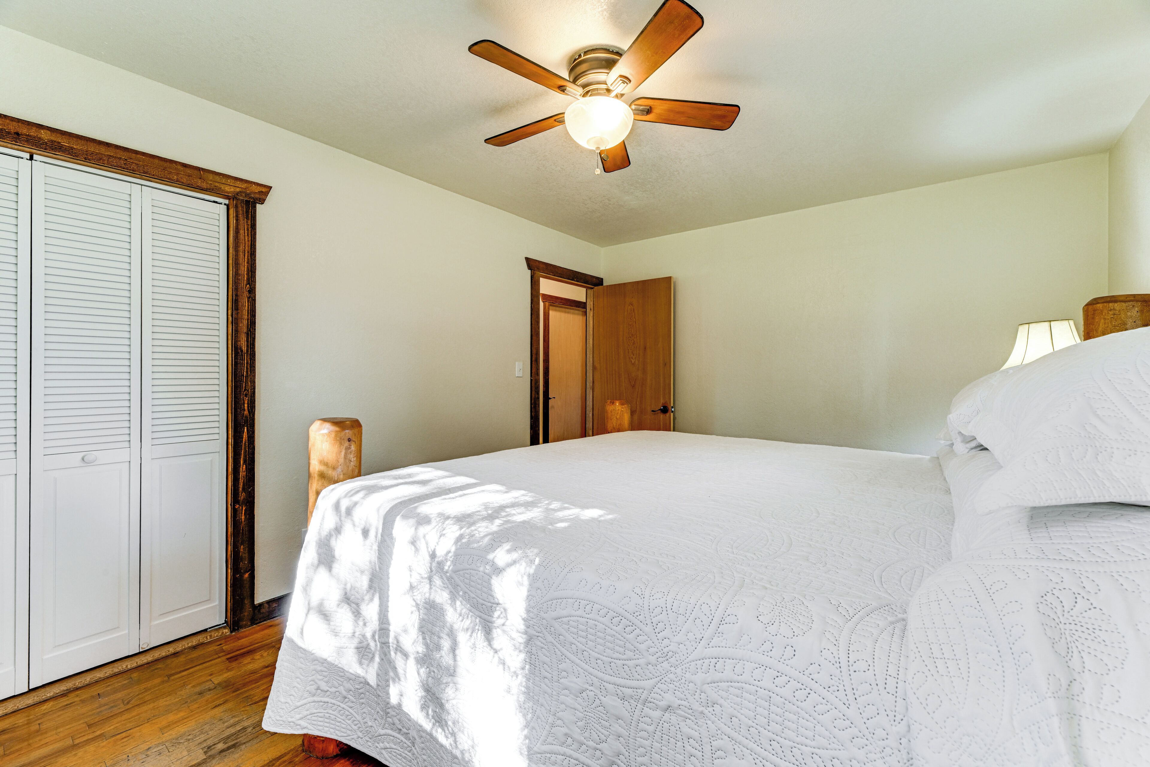 Un dormitorio con cama, ventilador de techo, puerta de madera y pared blanca.