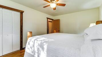 Un dormitorio con cama, ventilador de techo, puerta de madera y pared blanca.