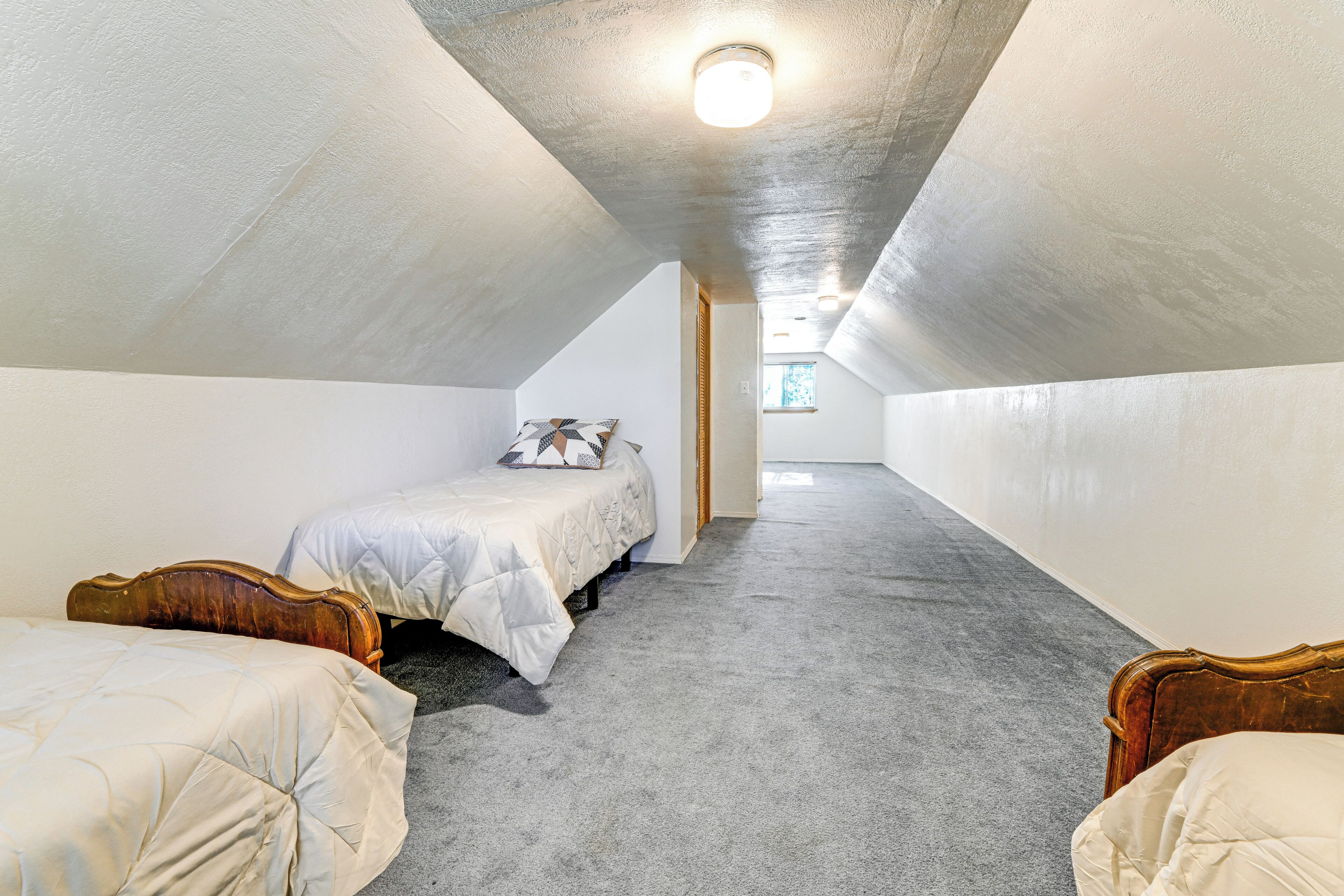 A bedroom with a sloped ceiling, a bed with a quilted cover, a bedside table, and a window.