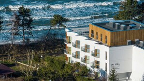 A modern building with a wooden facade and multiple balconies, located near a coastline with visible waves. - Navango - Beachfront, Sea View Pool & Sauna (Gąski)