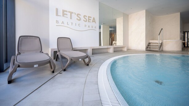 A modern indoor swimming pool area with two lounge chairs, a wall with 'LET'S SEA BALTIC PARK' signage, and a clear pool. - Navango - Beachfront, Sea View Pool & Sauna (Gąski)
