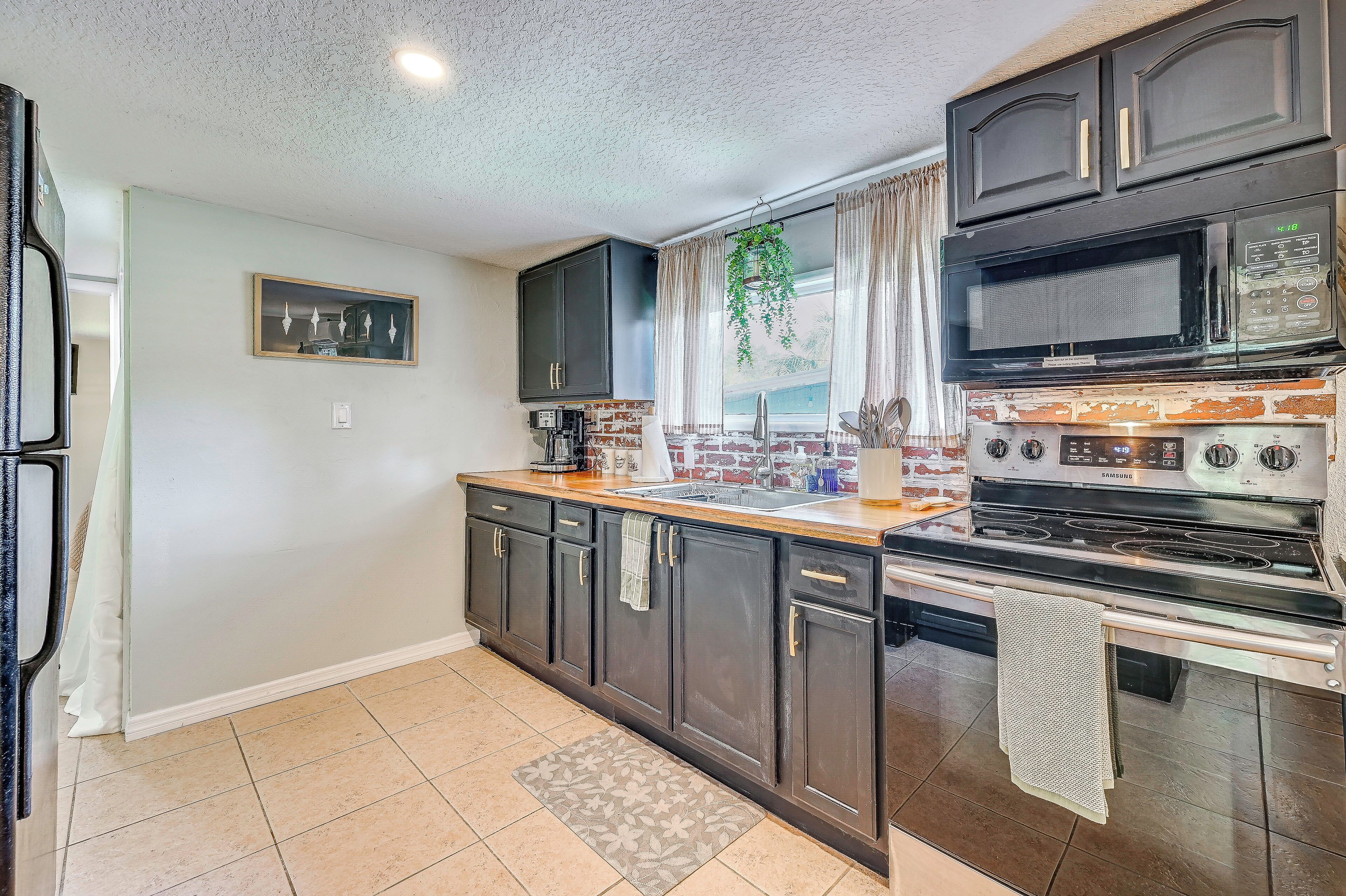 A kitchen with dark cabinets, a microwave, a stove, and a window with curtains.