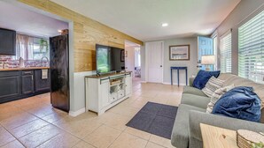 Una sala de estar con televisión, un sofá y una zona de cocina con refrigerador.