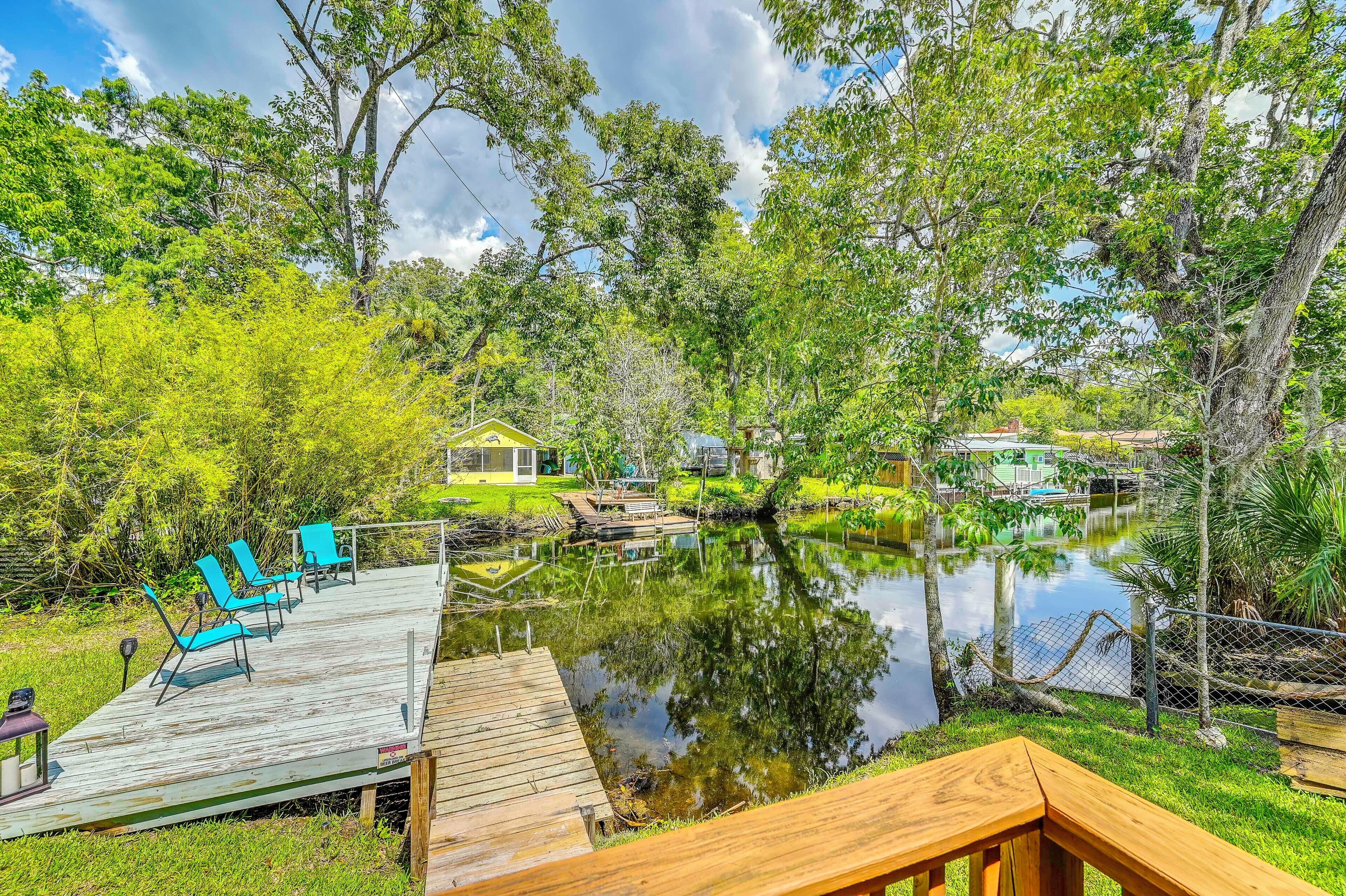 A wooden deck with chairs, a pond, and a small house with a yellow roof.