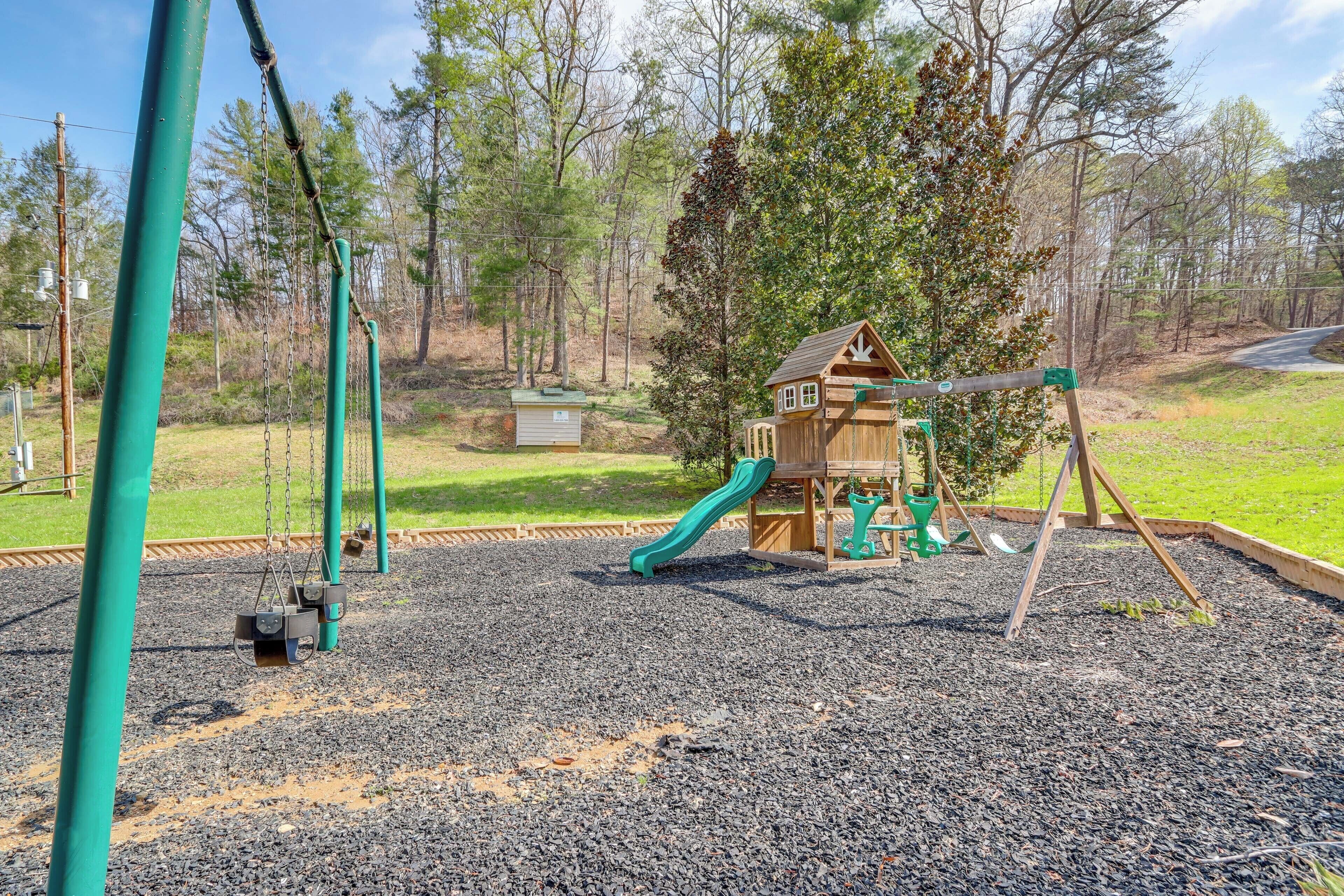 Un parque infantil con un tobogán de madera y columpios, rodeado de grava y árboles.