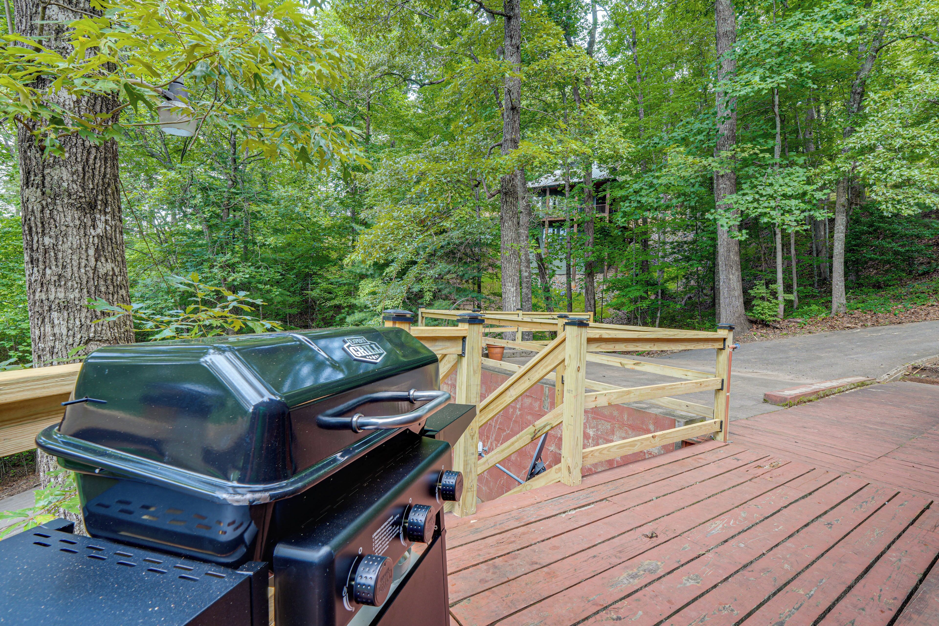 A barbecue grill on a wooden deck with a wooden fence in a wooded area.