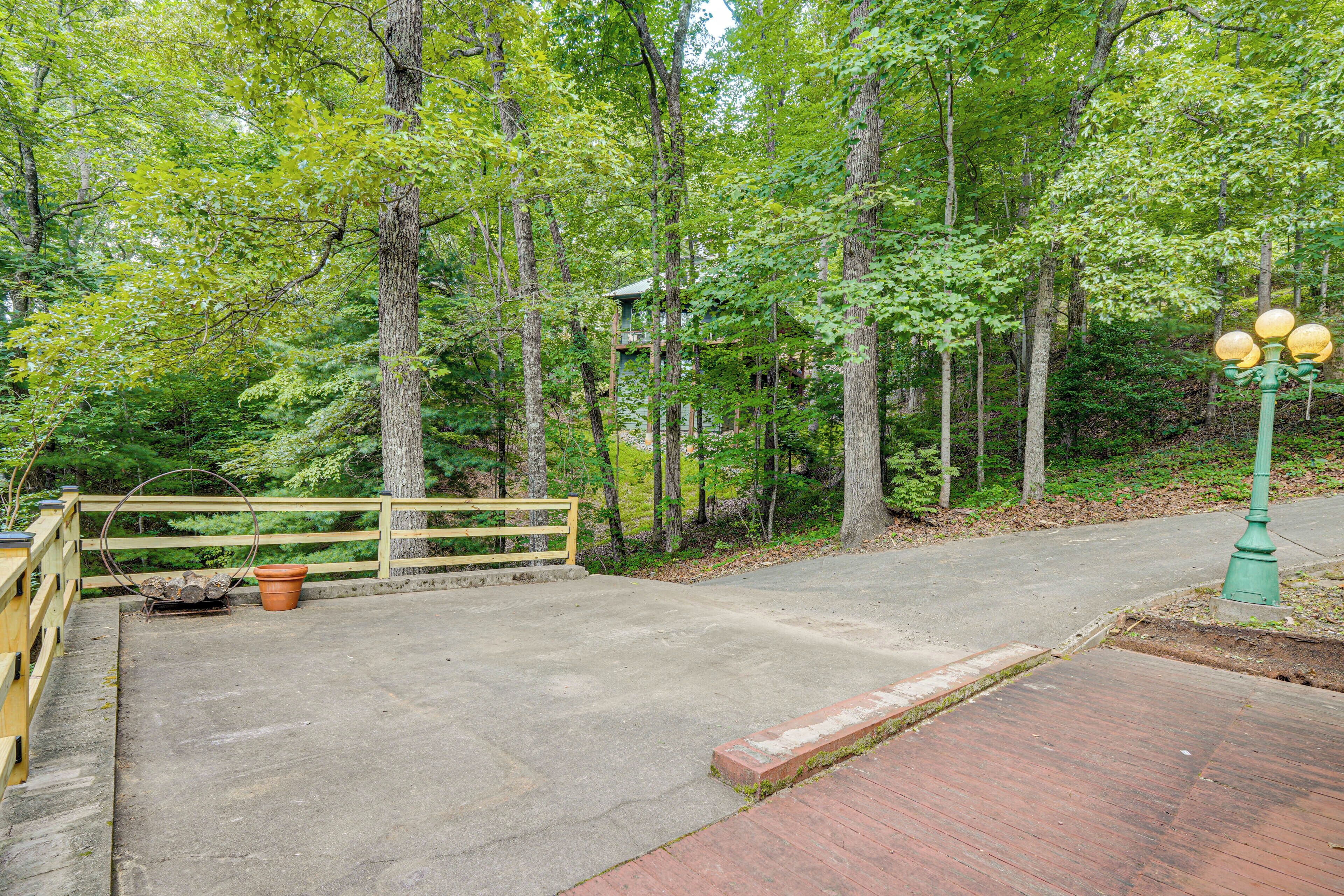 A paved pathway leading through a wooded area with a wooden fence and a lamp post.