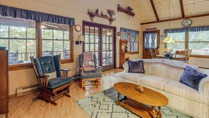A cozy room with a wooden ceiling, a large window, a sofa, a chair, and a coffee table. - Charming Resort Cabin at Lake Hiwassee! (Murphy)