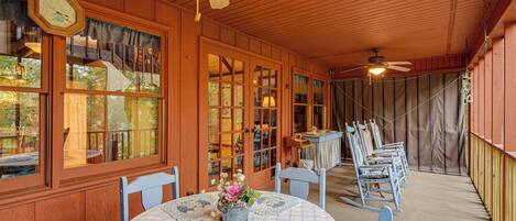 A wooden covered porch with a table and chairs, a clock, and a ceiling fan.