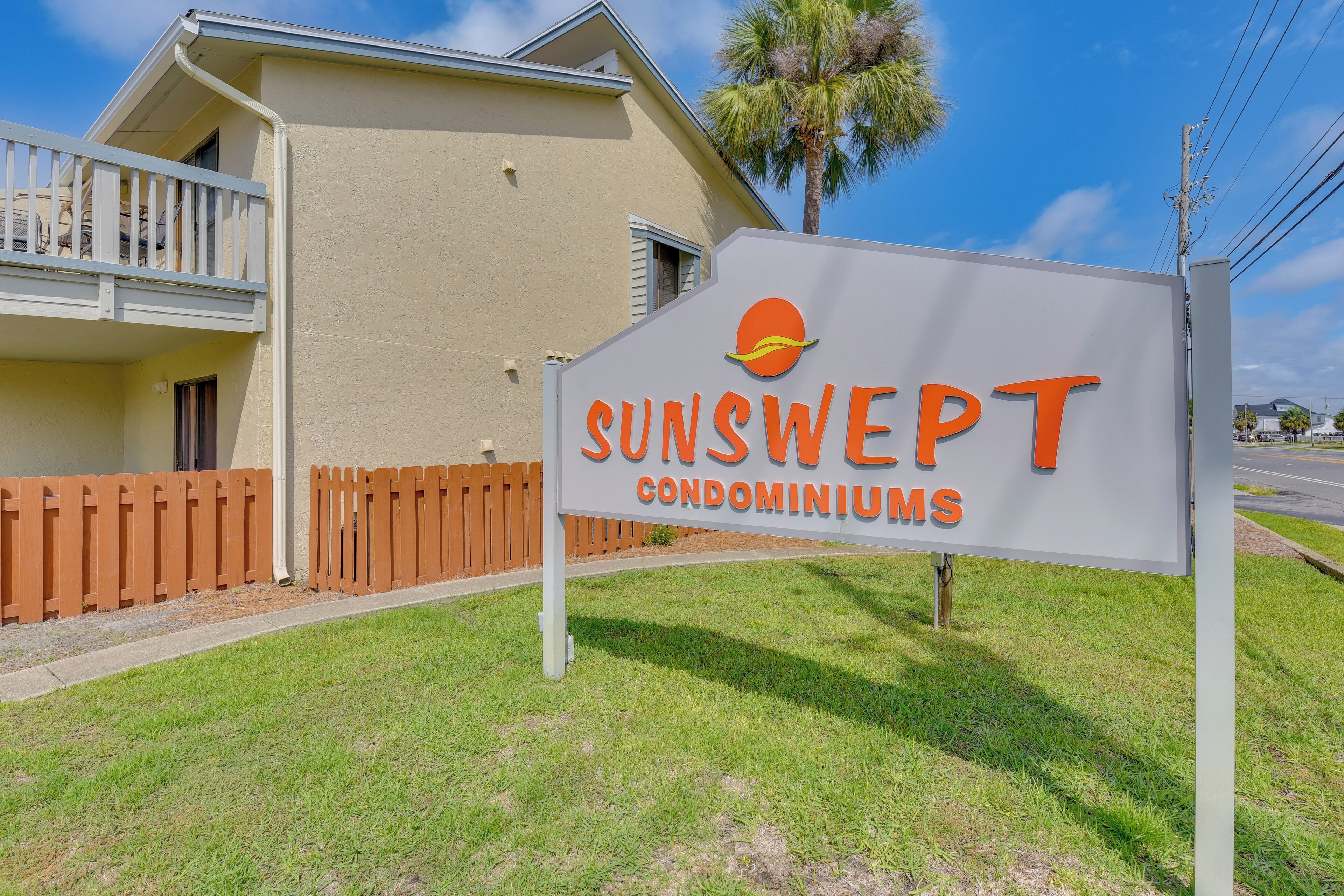 A sign for SUNSWEEP condominiums with a clear view of a building and a palm tree.