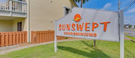 A sign for SUNSWEEP condominiums with a clear view of a building and a palm tree.