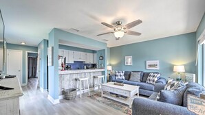 A modern living room with a grey sofa, a coffee table, and a kitchen area with white cabinets and a bar stool. - Steps to Beach! 2-unit Combo w/ Pool Access in PCB (Panama City Beach)