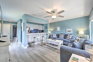 A modern living room with a grey sofa, a coffee table, and a kitchen area with white cabinets and a bar stool. - Steps to Beach! 2-unit Combo w/ Pool Access in PCB (Panama City Beach)