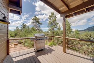 A wooden deck with a barbecue grill, overlooking a mountainous landscape.