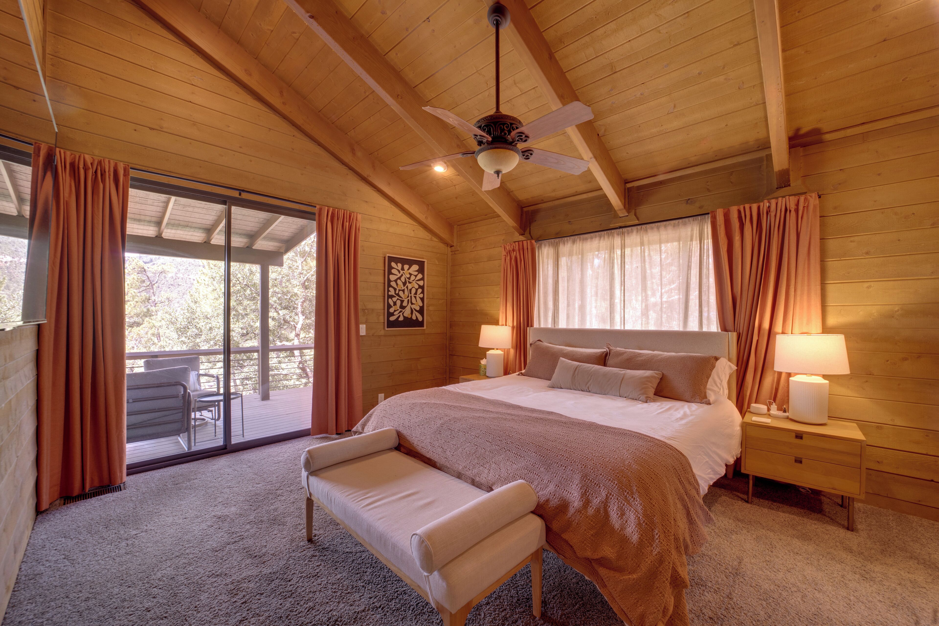 A cozy wooden room with a bed, a bench, and a ceiling fan.