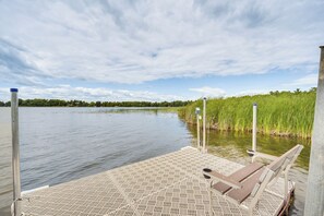 A wooden dock extending into a calm body of water with a grassy bank on one side and a cloudy sky above. - Dock, Fire Pit, Games! Spirt Lake Family Retreat (Frederic)