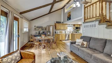 A spacious living area with a high ceiling, wooden beams, a dining table with chairs, a sofa, and a kitchen in the background.